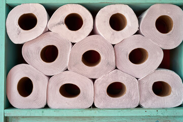 Pink toilet paper rolls stacking neatly on turquoise shelf, displaying organized bathroom supply...