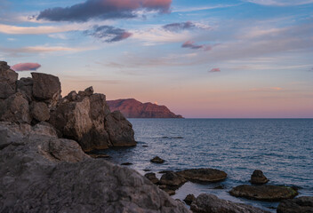 Sudak, Crimea Peninsula. View of the rocky shore of the Black Sea in the sunset light. Seascape with the rising Moon.