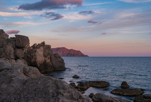 Sudak, Crimea Peninsula. View of the rocky shore of the Black Sea in the sunset light. Seascape with the rising Moon.
