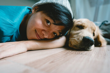 A real Asian man takes a selfie with a year-old golden retriever. The dog is licking its owner's face. Smiling People and fun playing together looking happily at the camera at home Pet and person