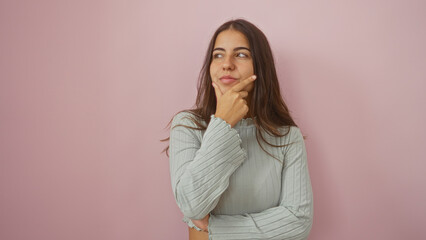 Woman thinking with hand on chin against a pink background expressing contemplation and curiosity...