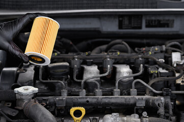 Auto mechanic holding car oil filter in hands on background of car engine compartment, close-up....