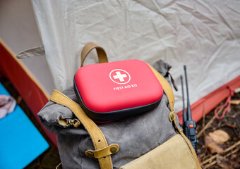 Red first aid kit on a backpack near a camping tent. Injuries and damage in the forest. Concept of...