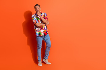 Confident young man with trendy style posing thoughtfully against vibrant orange background,...