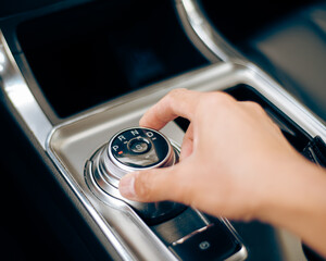 Asian man hand rotates rotary shifter gear shift knob at middle console of luxury SUV car in...