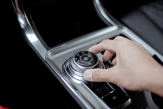 Asian man hand rotates rotary shifter gear shift knob at middle console of luxury SUV car in America, automatic transmission with shining metal dial gear selector of P, R, N, D and S Sport mode