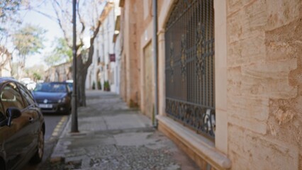 Mediterranean street scene with blurred background, defocused architectural details, cars parked along the sidewalk, and old town charm creating a serene, calm atmosphere.