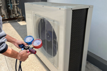 Air conditioning, HVAC service technician using gauges to check refrigerant and add refrigerant.	