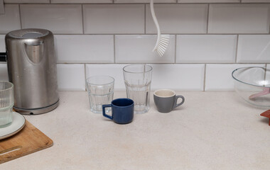dirty kitchen countertop with cluttered dishes glassware and electric kettle standing near white...