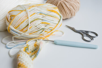 Colorful yarn balls and crochet hook with scissors on white background