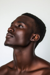 Obraz premium Close-up, low-key studio portrait of a young African man with dark skin. The subject is captured in profile, his head tilted upwards, gaze directed towards an unseen point above. The image features