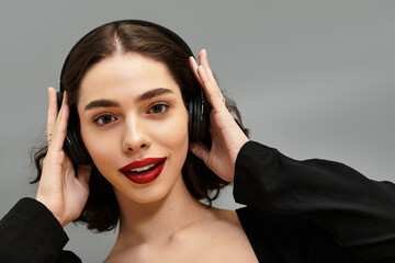 Fototapeta premium Young woman with striking red lips and braces enjoying music on a grey backdrop