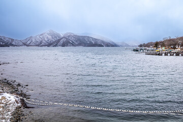 Lake Chuzenji, on the mountains in Nikko, Japan, during winter season with snow fall under cloudy sky and very cold weather. Japanese letters were name of public gate in Japanese faith.