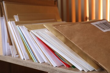 Different paper envelopes on wooden shelf in post office, closeup