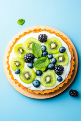 Delicious kiwi tart with fresh berries on wooden plate