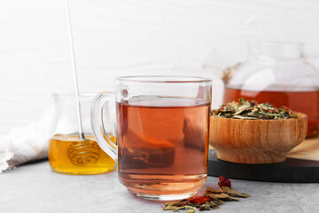 Delicious herbal tea with honey and dry leaves on grey table