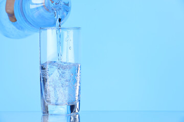 Man pouring soda water from bottle into glass on light blue background, closeup. Space for text