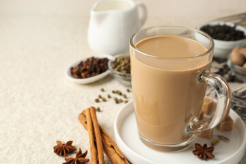 Aromatic Masala tea in glass cup, spices and brown sugar on white textured table, closeup. Space for text