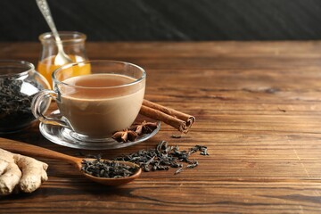 Aromatic Masala tea in cup, spices, dry leaves and honey on wooden table, closeup. Space for text