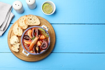 Delicious seafood soup in bowl, pieces of bread, lime and spices on blue wooden table, flat lay. Space for text