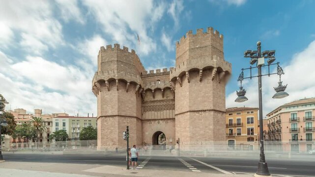 Serrans Towers (Torres de Serranos) timelapse hyperlapse in Valencia, Spain. A grand medieval gate from the city's ancient walls. Bustling street scene under a cloudy sky frames this historic landmark