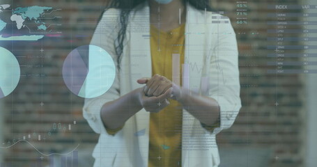 Image of financial data processing over businesswoman disinfecting hands