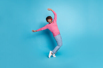 Happy young man in a pink sweater posing against a bright blue background, showcasing a cheerful...