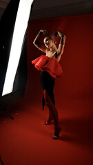 Portrait of sexy photo model posing in red dress and black transparent gloves. Luxurious girl on red background.