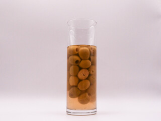 Glass cup filled with green olives, on white background, front view