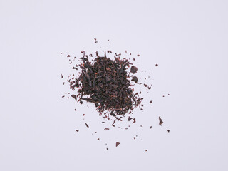 A pile of dry black tea leaves, on a white surface, top view