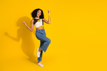 Stylish young woman in casual outfit posing gracefully on vibrant yellow background, expressing...