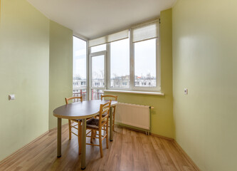 Small dining area with wooden table and chairs, near a window with city view. Light green walls and wooden floors.