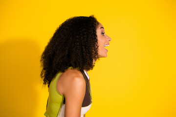 Playful young woman with curly hair on yellow background enjoying a cheerful moment and expressing...