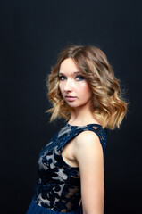 Fototapeta premium Woman in blue dress with lace pattern posing in studio on dark background. Close-up portrait.