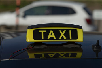 The taxi sign is prominently placed on top of a car roof, set against a bustling urban background