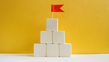 Wooden cubes forming pyramid with red flag on top. Achievement, business success. Yellow backdrop