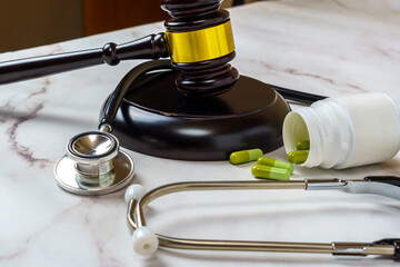 Wooden judge's hammer next to a pack of pills and a stethoscope on a table. Right to ensure access...