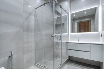 A modern shower cabin with glass sliding doors in the interior of the bathroom, decorated in white.