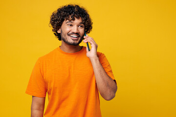 Young happy Indian man he wears orange t-shirt casual clothes talk speak on mobile cell phone...