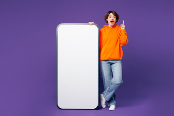 Full body young woman she wears orange hoody casual clothes big huge blank screen mobile cell phone...