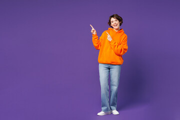 Full body young smiling cheerful fun cool happy woman wear orange hoody casual clothes point index...