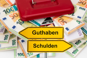 Vor einer Geldkassette mit vielen Bündel Euro Banknoten steht ein Wegweiser beschriftet mit...
