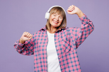 Elderly blonde woman 50s years old wears violet shirt casual clothes listen to music in headphones...