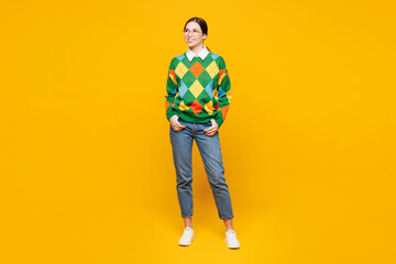 Fototapeta premium Full body young smiling happy smart woman she wear glasses green sweater casual clothes stand look aside on area mock up isolated on plain orange yellow background studio portrait. Lifestyle concept.