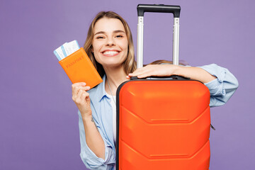 Close up traveler woman wear blue clothes hold passport ticket suitcase bag isolated on plain purple background. Tourist travel abroad in free spare time rest getaway. Air flight trip journey concept.