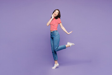 Full body side view young woman wear red striped t-shirt casual clothes point hand on face raise up leg look camera isolated on plain pastel light purple background studio portrait. Lifestyle concept.