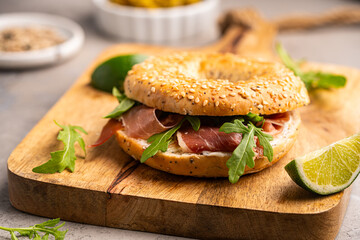 Sandwich with ricotta, prosciutto and microgreens, bagel with ham for breakfast on gray background, close up.