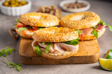 Variety of Bagel sandwiches with ricotta, prosciutto or chicken ham or salmon and microgreens, bagel with ham for breakfast on gray background, close up. Healthy breakfast food.