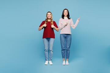 Fototapeta premium Full body young couple two friends women wearing red casual clothes together point index finger aside on area mock up show thumb up isolated on pastel plain light blue background. Lifestyle concept.