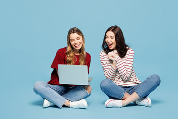 Full body young surprised couple two IT friends women wear red casual clothes together sit hold use work on laptop pc computer isolated on pastel plain light blue cyan background. Lifestyle concept